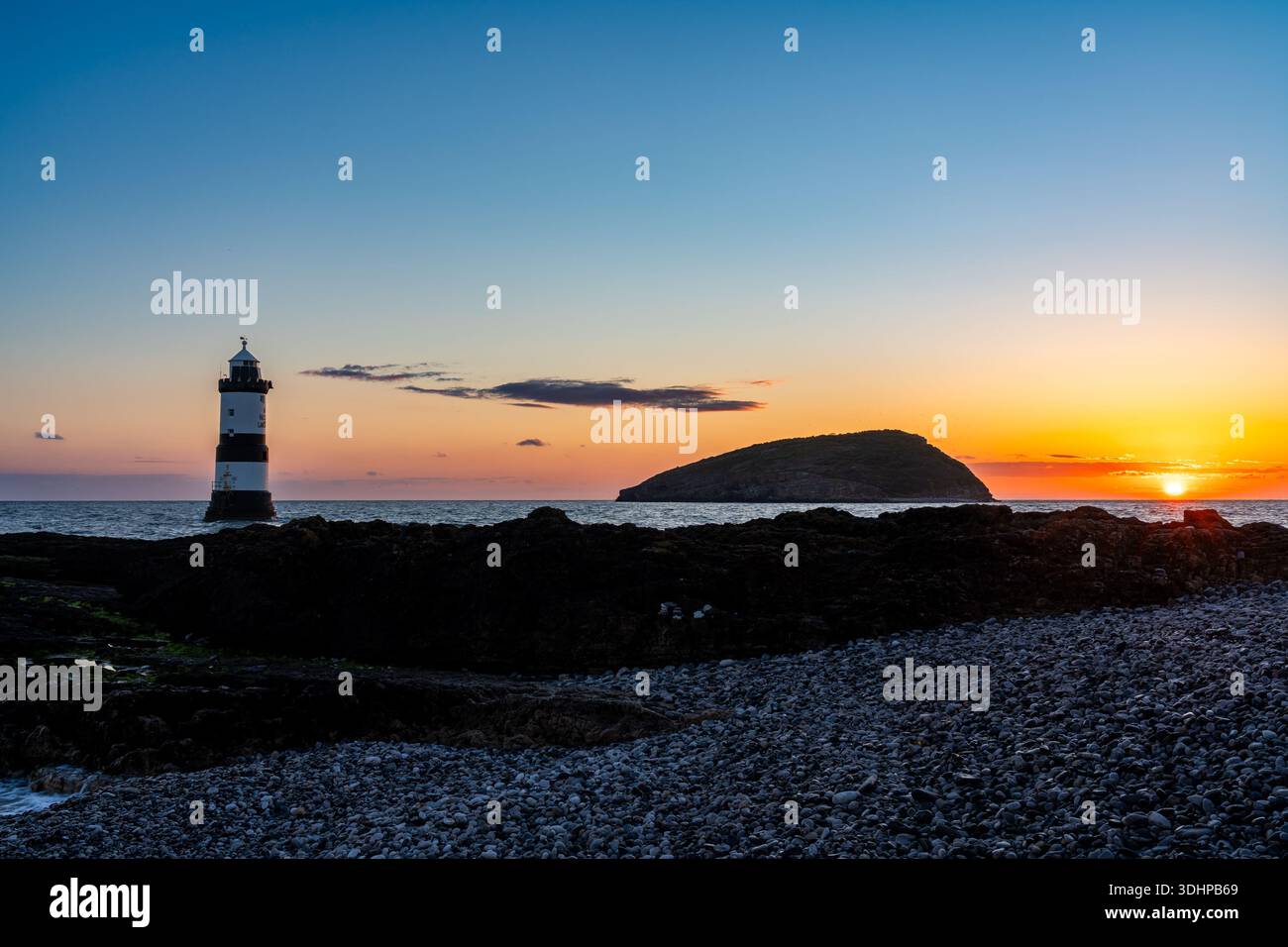 Sonnenaufgang am Penmon Point mit Trwyn du Lighthouse und Puffin Island am Horizont Stockfoto