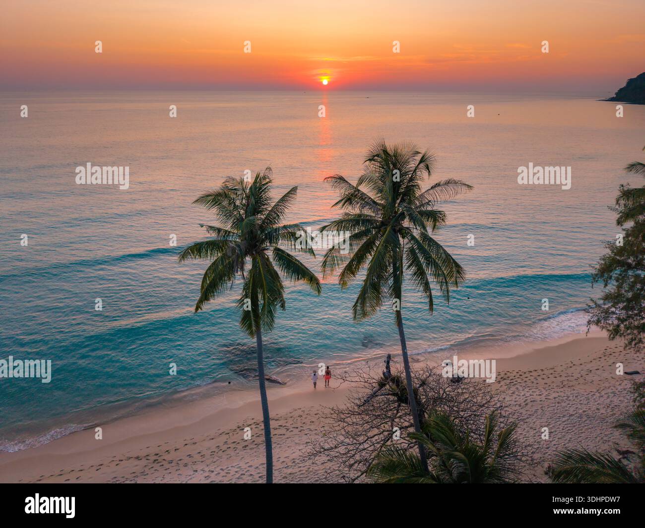 Erleben Sie die ruhige Schönheit des Takhian Beach in Koh Kood, Thailand, während sich die leuchtenden Farben des Sonnenuntergangs auf dem ruhigen Wasser spiegeln. Ein paar Männer und ein AA Stockfoto