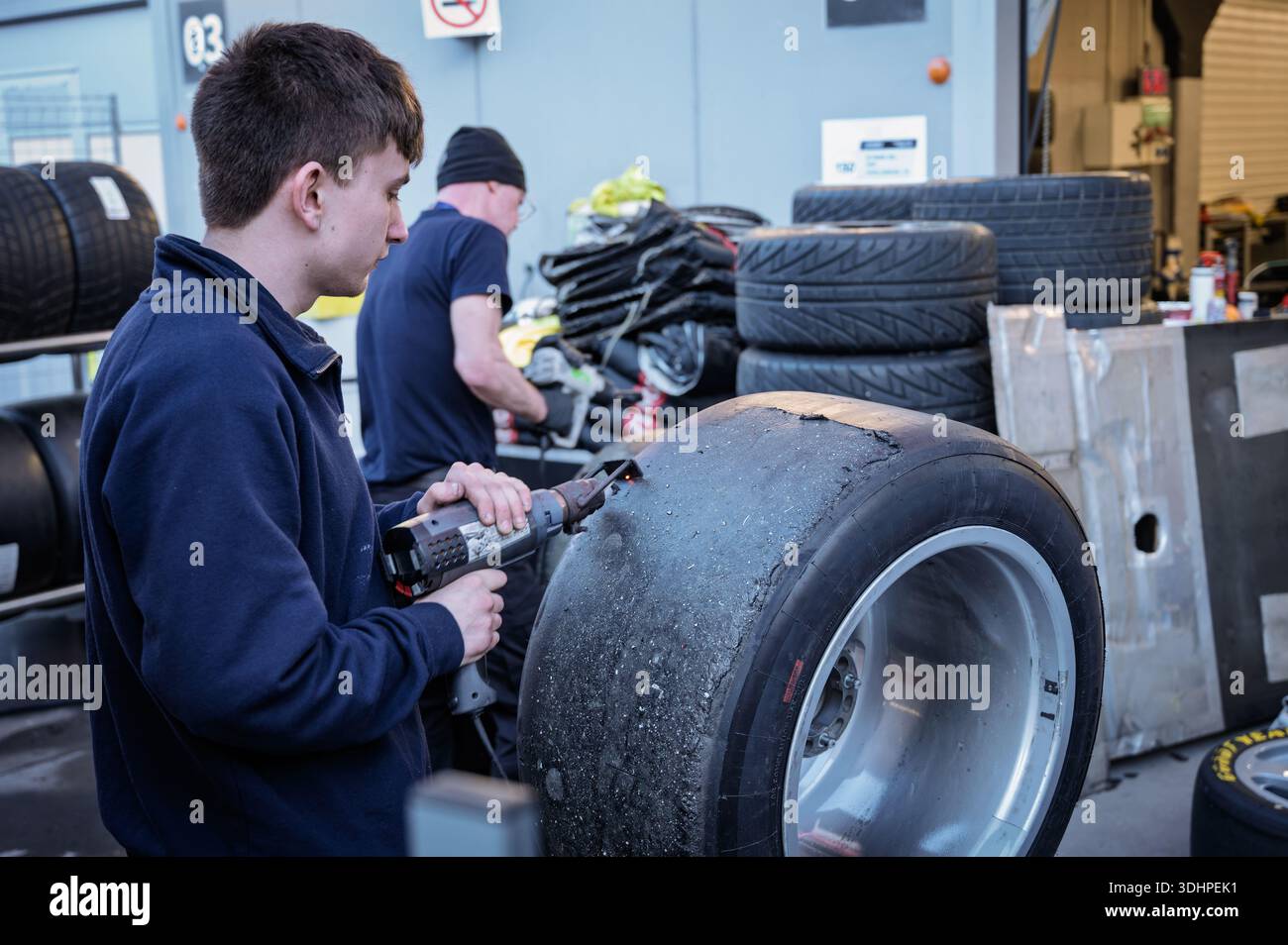 Ein junger Mechaniker aus dem Rennteam Pits reinigt mit einer Heißluftpistole einen glatten Reifen, der mit Körnung bedeckt ist Stockfoto