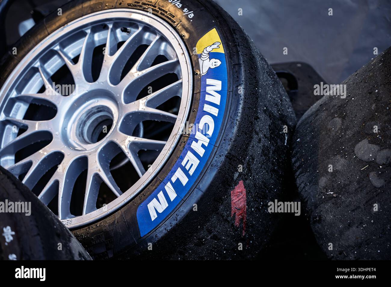 Detaillierte Nahaufnahme nasser, gestapelter Rennwagenräder mit Michelin Slick-Reifen und einer Rennfelge mit nur einer Mutter Stockfoto