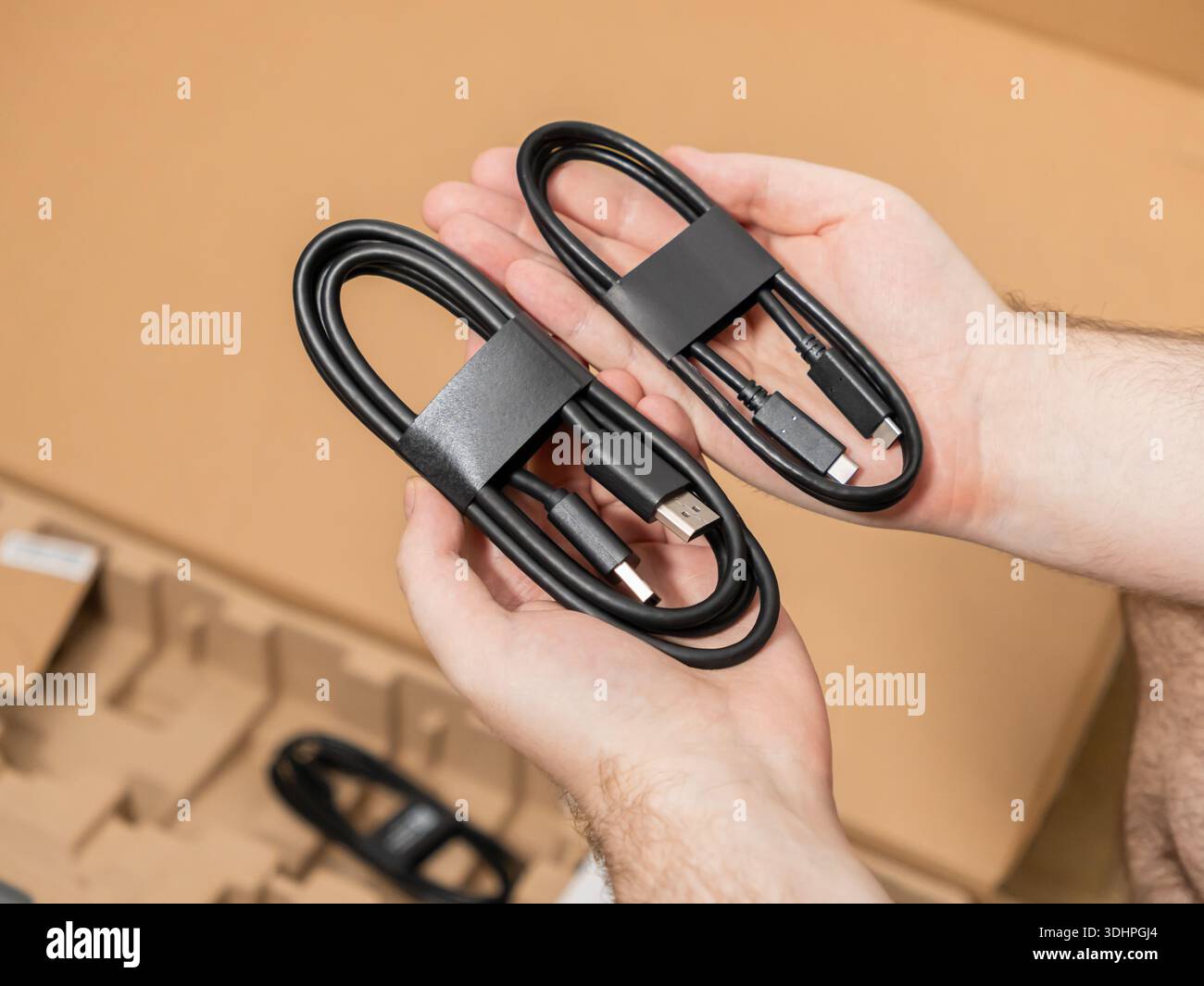 Nahaufnahme der Hände mit zwei wichtigen schwarzen USB-Kabeln, einschließlich Typ-C auf Typ-C und Typ-A auf Typ-C, ideal zum Auspacken neuer Technologien Stockfoto