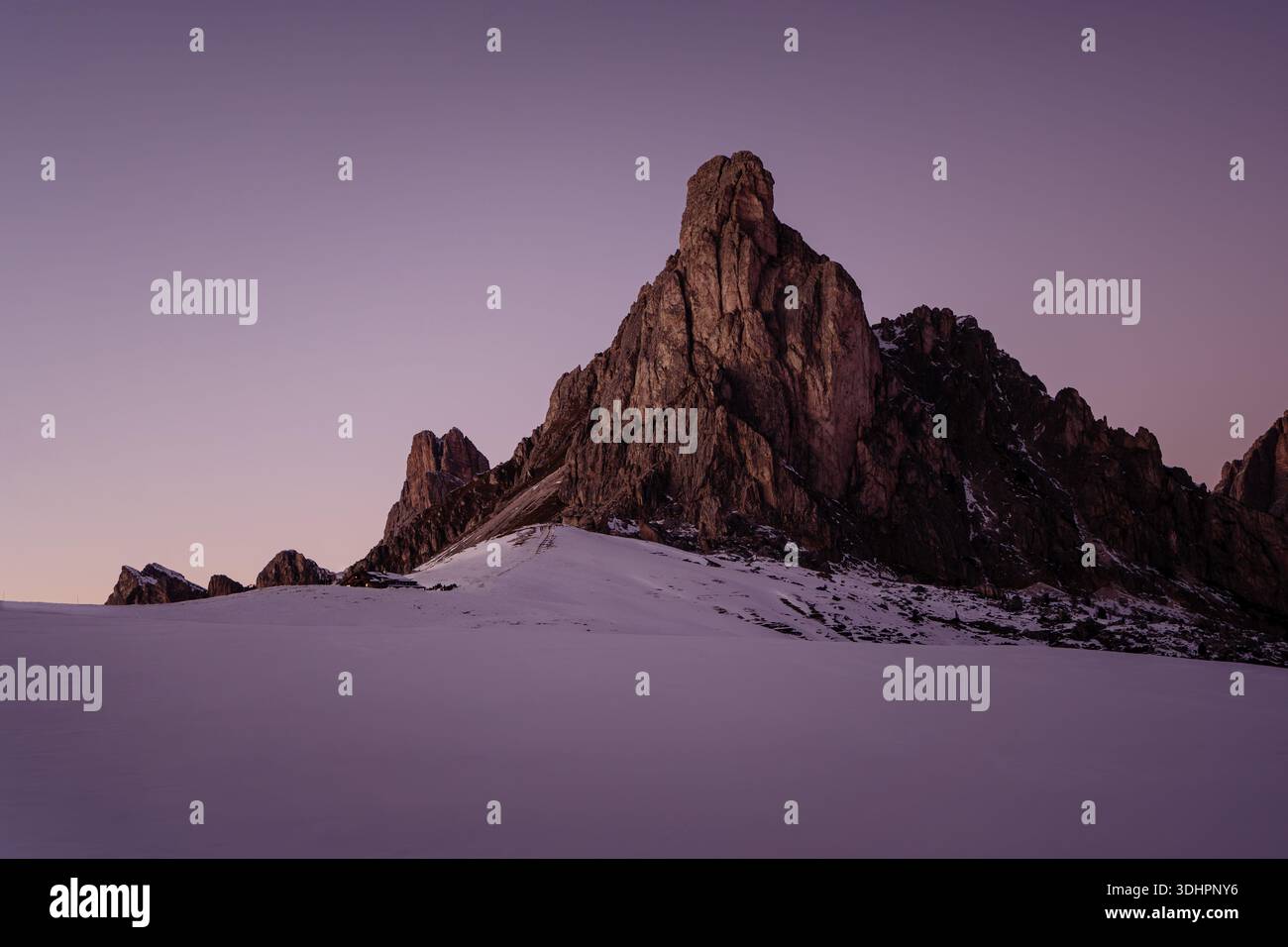 Wintersonnenuntergang am Passo Giau in den Dolomiten, wo warme alpine Lichter mit schneebedeckten Gipfeln unter einem dramatischen violetten Himmel kontrastieren. Stockfoto