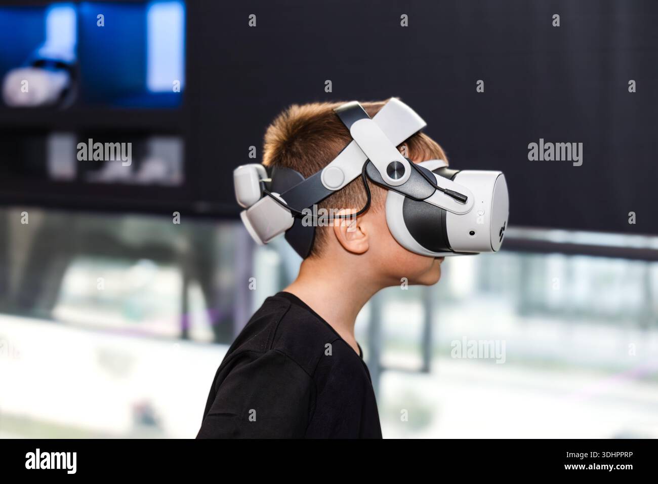 Ein Kind, das eine VR-Brille trägt, hält einen Controller, während er tagsüber einen virtuellen Raum in einem Spielcenter erkundet Stockfoto