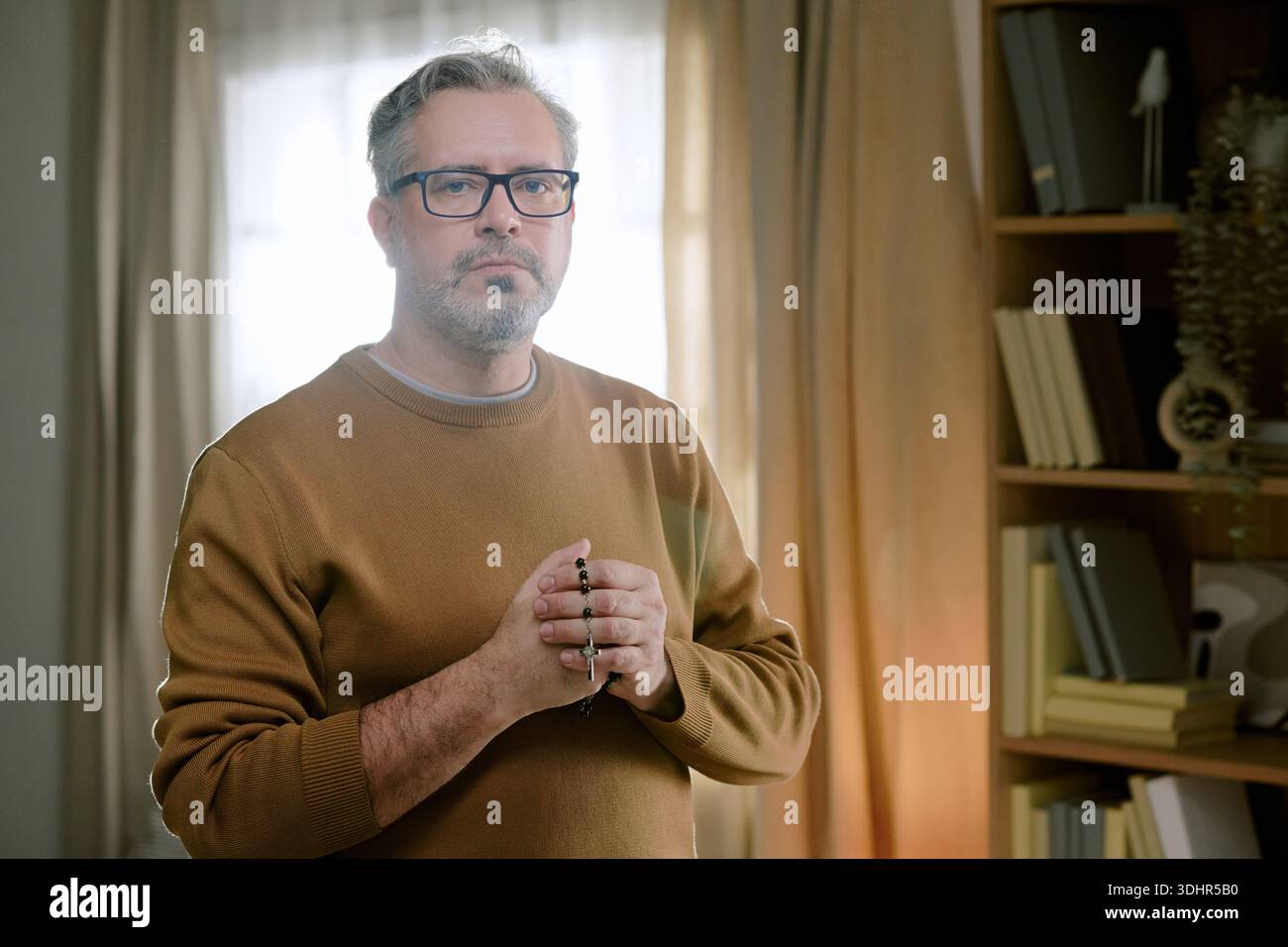Porträt eines Mannes mittleren Alters, der drinnen steht und Rosenkranzperlen hält Stockfoto