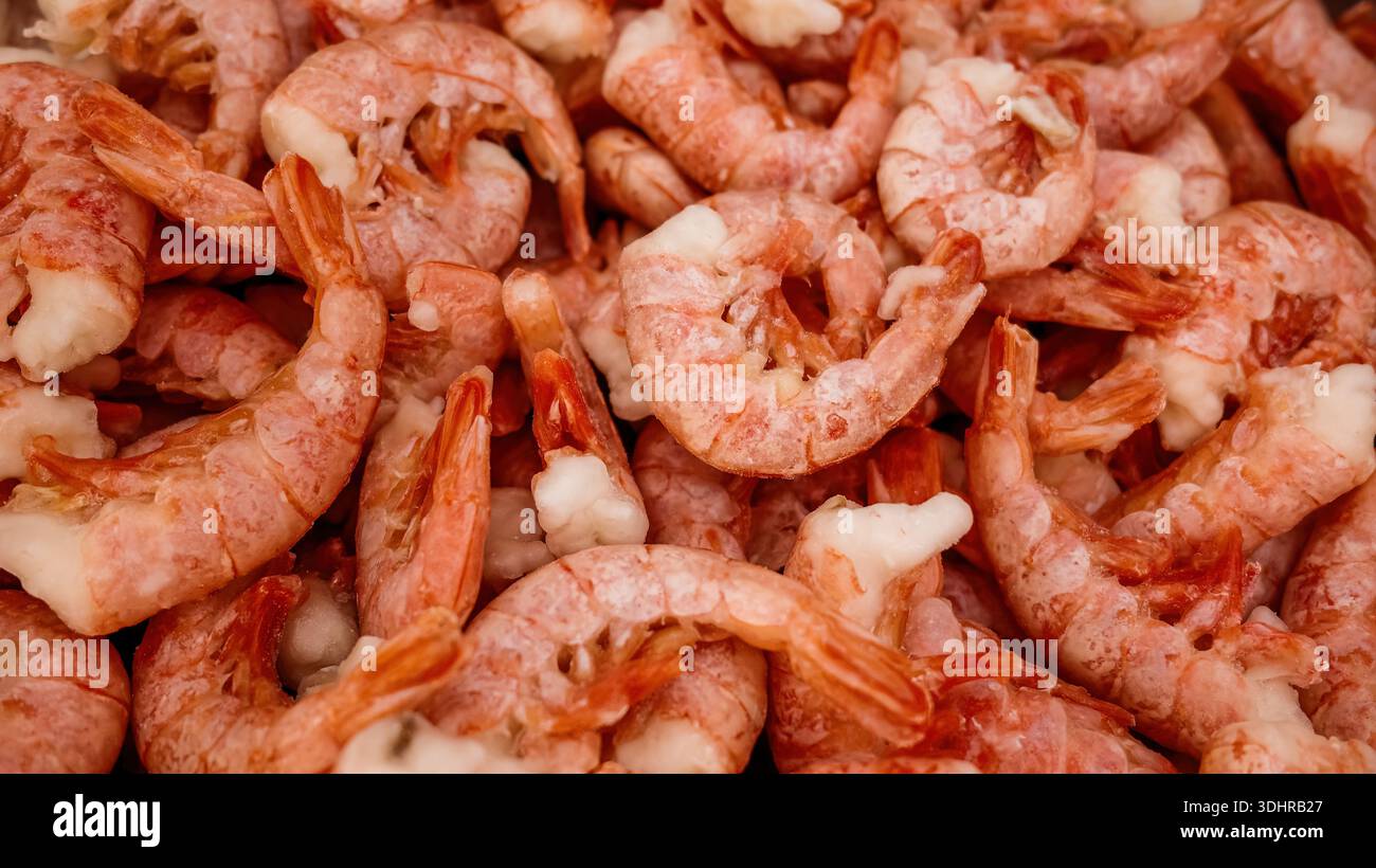 Gefrorene ungeschälte Garnelen Meeresfrüchte Hintergrund. Haufen gefrorener roher, ungeschälter Garnelen mit Muscheln, Texturhintergrund für Meeresfrüchte für Marktpräsentation, Verpackung Stockfoto