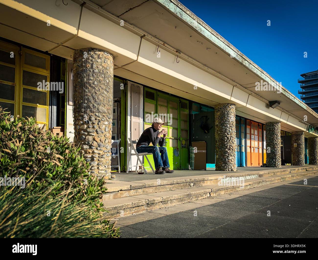 Eine Künstlerin sitzt morgens vor ihrem Studio am Strand in Worthing - Smartphone-aufgenommenes Stockfoto