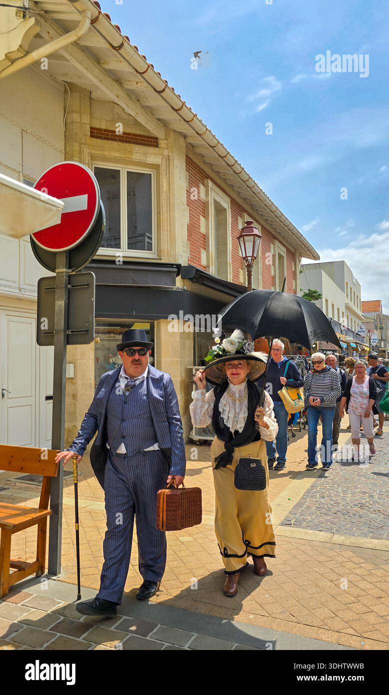 Soulac-sur-Mer, Frankreich - 8. Juni 2025. Ein bezauberndes Paar mittleren Alters in Kostümen der Belle Epoque mit schwarzem Schirm spaziert auf dem jährlichen fest durch die Straße Stockfoto