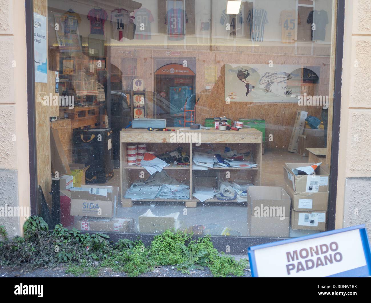Cremona, Italien 9. Januar 2026 Schaufenster mit einem unorganisierten Arbeitsbereich im Inneren, mit hängenden Sportrikots und Außenreflektionen, mit einem Mo Stockfoto