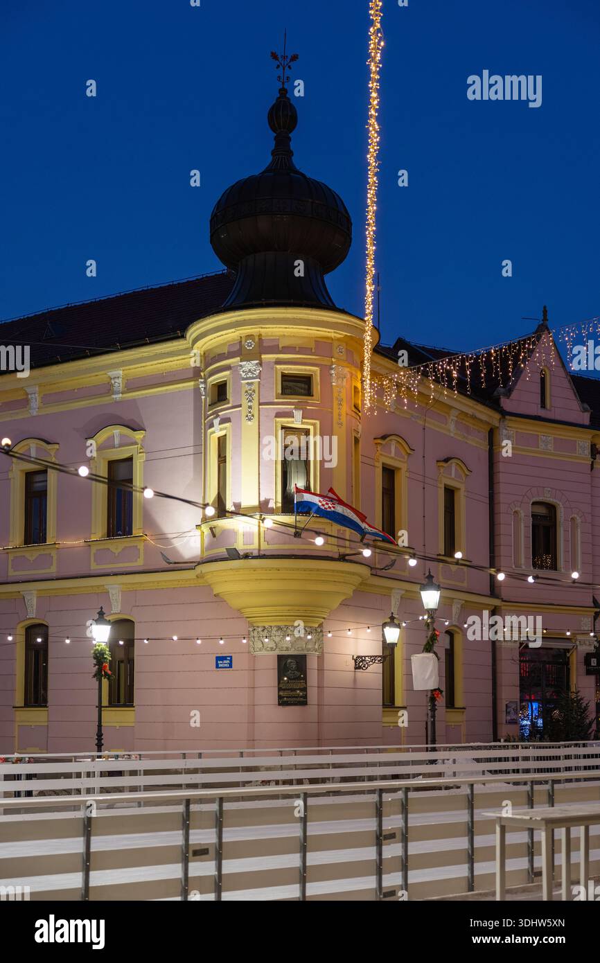 Eine bezaubernde urbane Szene in der Dämmerung mit einem pinkfarbenen Eckgebäude, Lichterketten, einem Kuppelturm und Flaggen. Warmes Leuchten von Straßenlaternen erzeugt ein fe Stockfoto