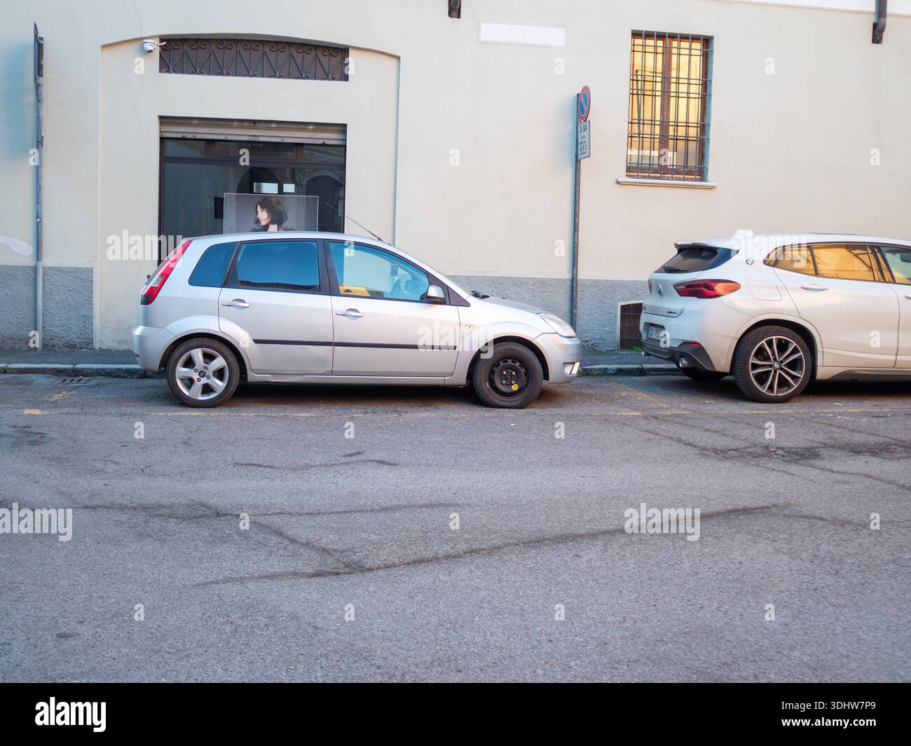 Cremona, Italien 9. Januar 2026 Alte und neue Autos stehen im Kontrast zu einem kompakten silbernen Ford Fiesta auf einem temporären Reserverad, das dicht hinter einem modernen W geparkt ist Stockfoto