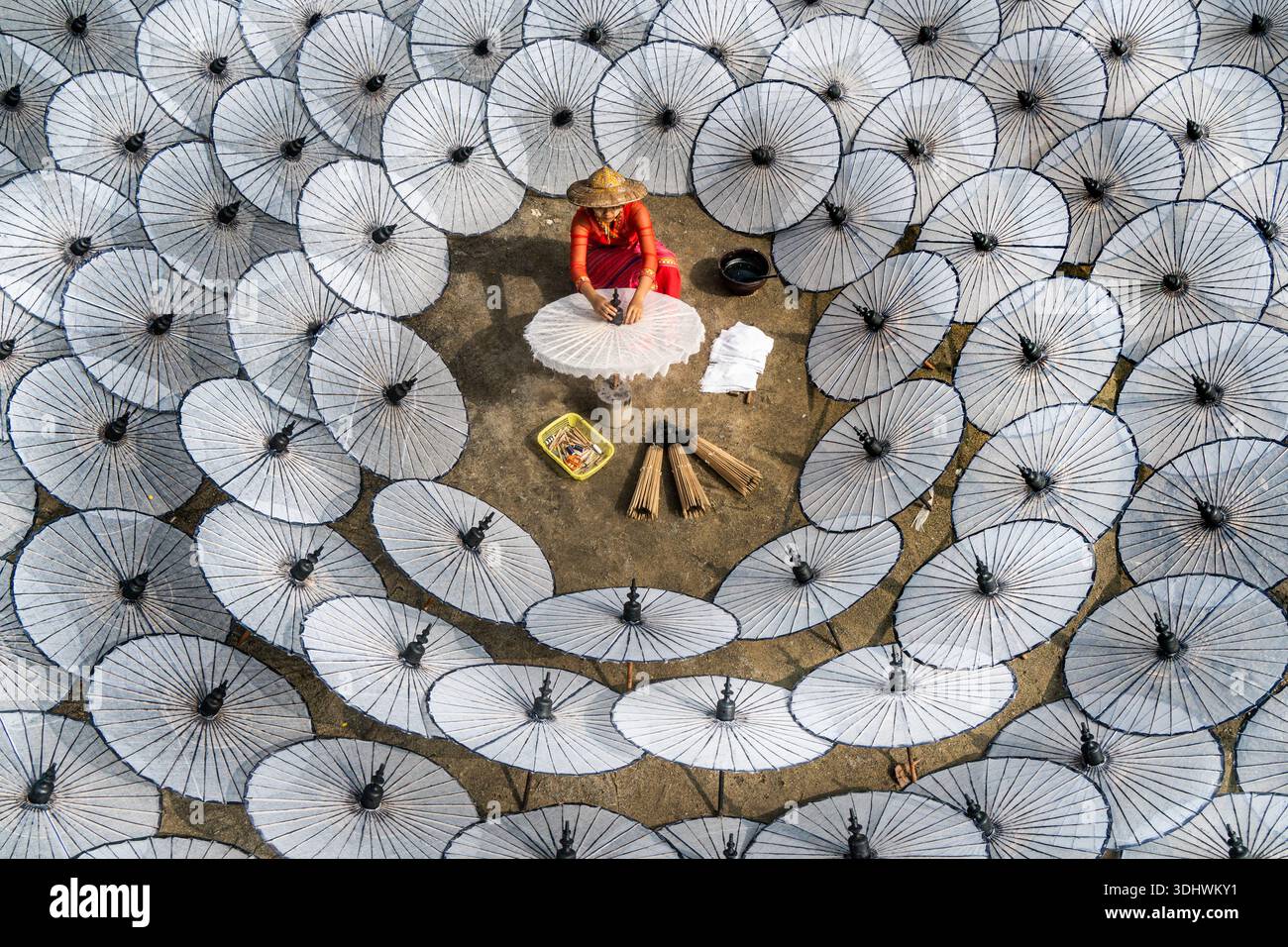 Blick auf eine Handwerkerin in leuchtendem Rot, in einem Meer von weißen Papierschirmen, die einen auffälligen Kontrast von Farbe und Textur schaffen, Mandalay, Manda Stockfoto