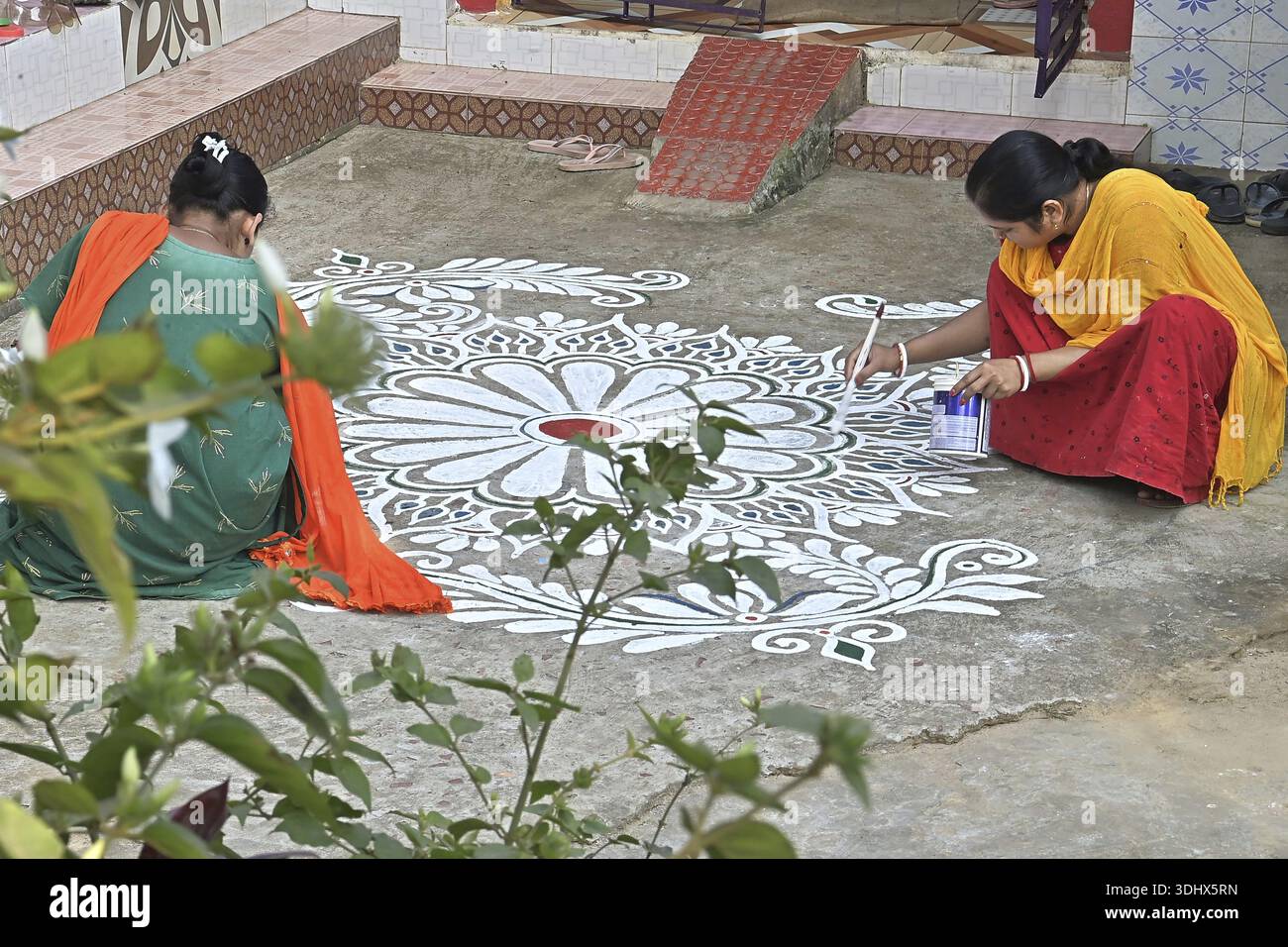 Agartala, Tripura, Indien, 12.01.2026: Frauen malen Alpona auf dem Boden vor dem Hindu-Festival Makar Sankranti im Dorf Lankamura in Agartala. Stockfoto