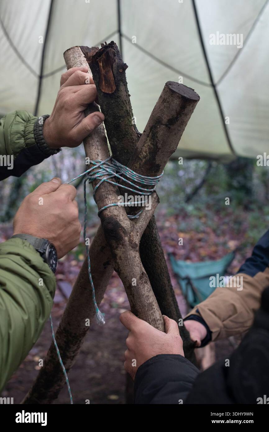 Überlebenskurs, Überlebensmethoden im Freien. Bau eines Outdoor-Kochstativs mit Holzstangen und Seilen. Stockfoto
