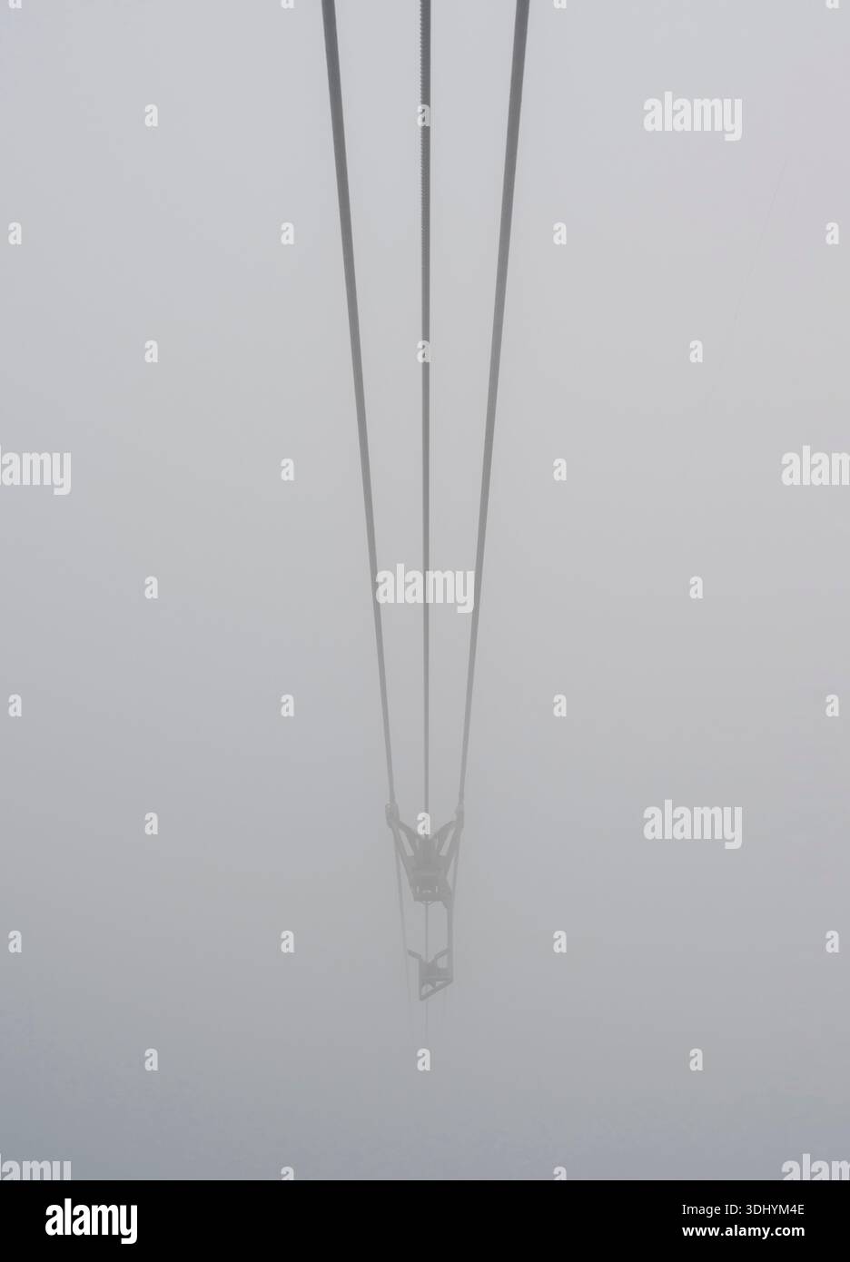 Drei parallele Kabel führen senkrecht in dichten Nebel ab und schaffen eine minimalistische Komposition mit starker linearer Perspektive. Der Nebel verdeckt den Hintern Stockfoto
