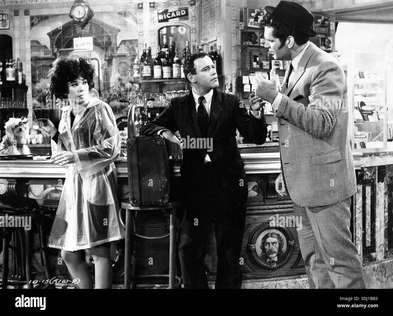 In dieser 1963 erschienenen Schwarzweiß-Werbung aus dem Film „Irma la Douce“ wird Jack Lemmon als Nestor Patou dargestellt, der sich mit einem anderen Mann unterhalten hat, wahrscheinlich in einer Bar oder einem Café in Paris. Eine Frau in einem durchscheinenden Regenmantel, Shirley MacLaine als Irma, steht links und trägt zur lebhaften Atmosphäre der Szene bei. Stockfoto