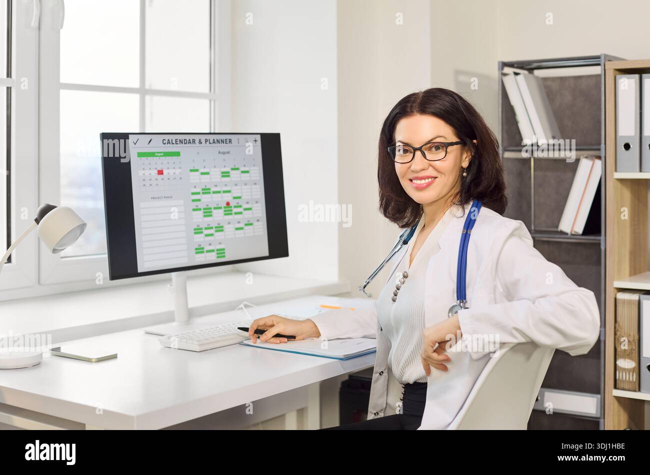 Lächelnde Ärztin im Klinikbüro, die Termine auf dem Desktop-Computer festlegt Stockfoto