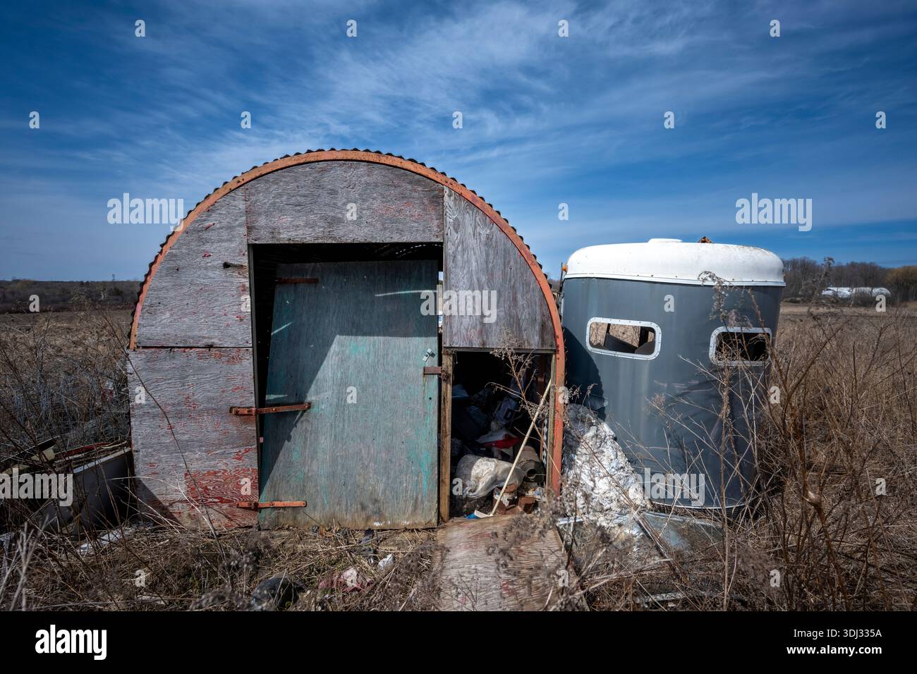 Verlassene Farm Deponie mit heruntergekommenem Schuppen und Vintage-Wohnwagen in offener Landschaft, die an ländliche Verfall und die ruhige Romantik der Ruine erinnern. Stockfoto