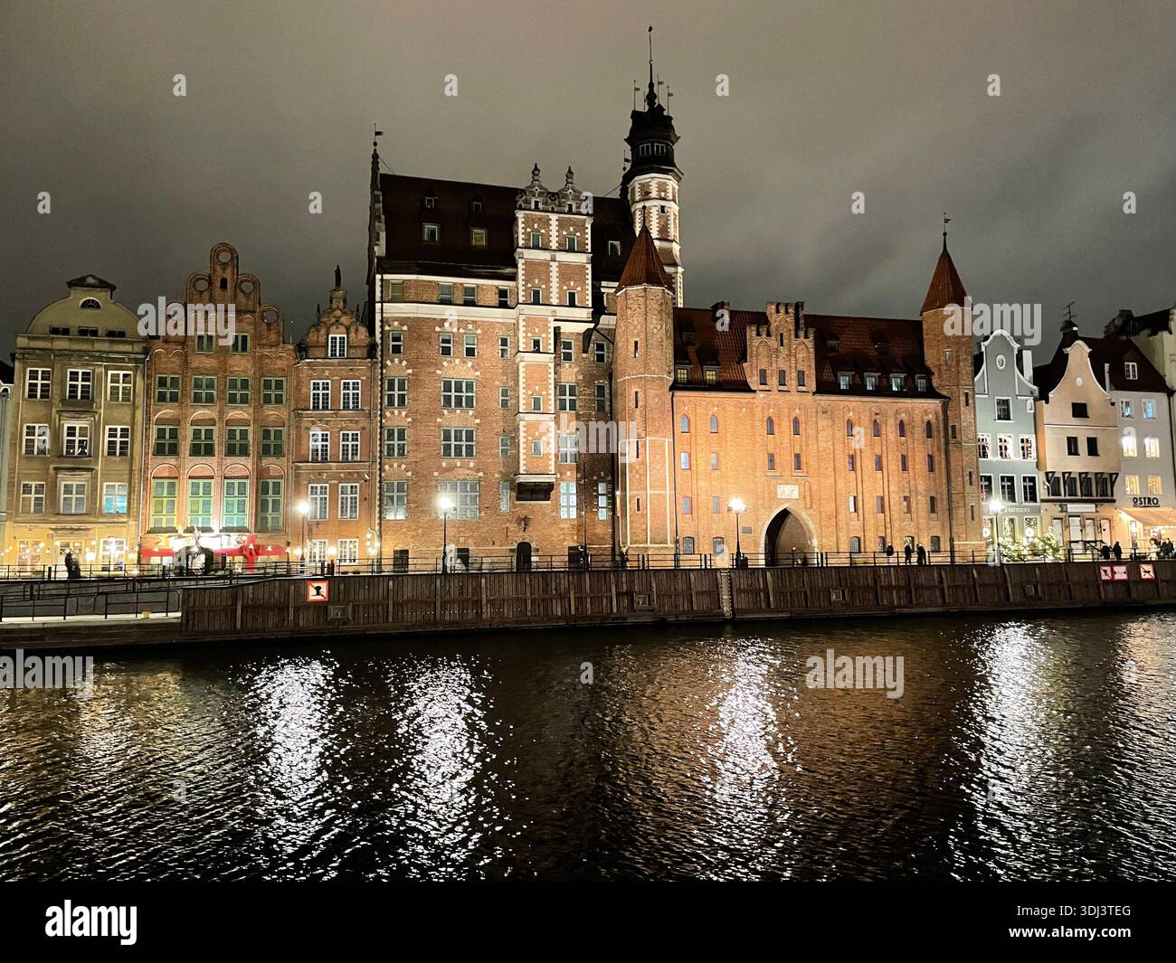 Beleuchtete historische Gebäude am Ufer des Flusses Motława in Gdańsk, Polen, die sich während einer ruhigen abendlichen Stadtszene im Wasser spiegeln - Smartphone-aufgenommenes Stockfoto
