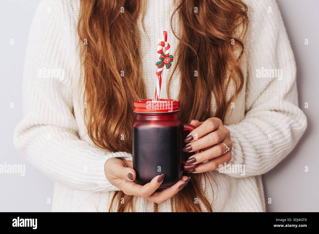 Frau, die ein Glas mit hausgemachtem Getränk und dekorativem Stroh hält. Warmes Wintergetränk, zubereitet zu Hause. Gemütlicher Lifestyle und saisonale Erfrischungen. Stockfoto