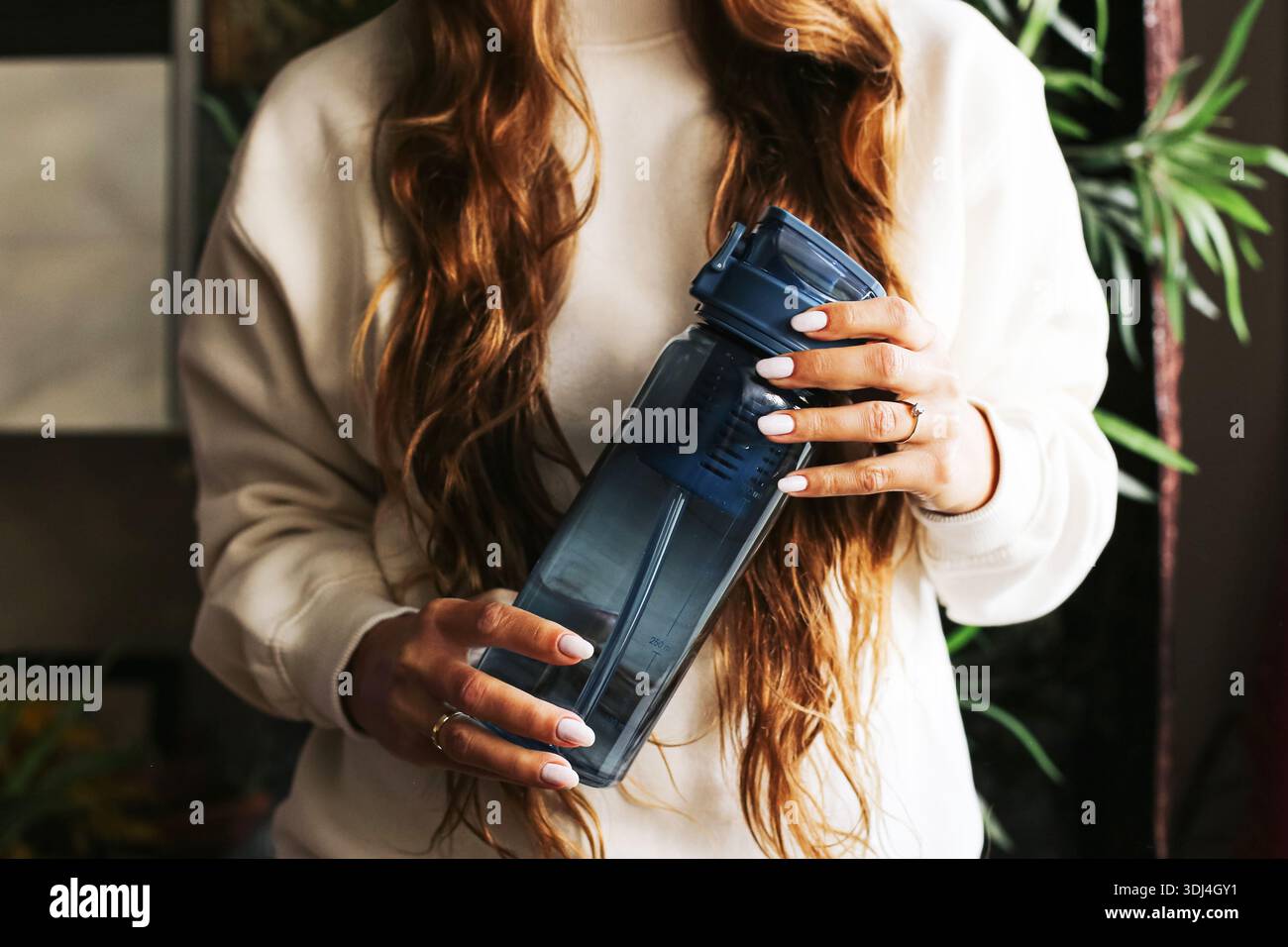 Frau, die eine wiederverwendbare Wasserflasche in Innenräumen hält. Hydratation und gesundes Lifestyle-Konzept. Nachfüllbarer umweltfreundlicher Behälter in weiblichen Händen. Stockfoto