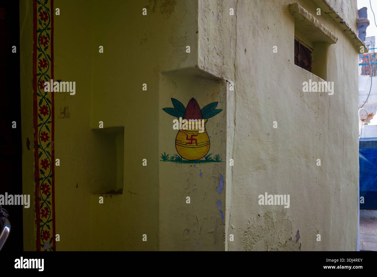 Bundi, Indien - 19. März 2022: Ein gemaltes Bild eines kalash-Topfes mit Blättern und einem Hakenkreuz-Symbol ist an einer gelben Wand an der Ecke eines Gebäudes zu sehen, mit einem dekorativen Blumenrand am Rand. Stockfoto