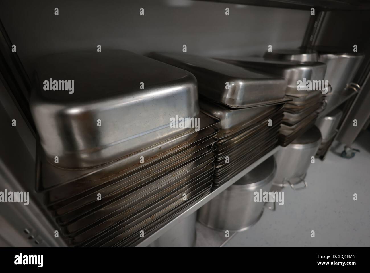 Details mit Küchentöpfen, Pfannen und Utensilien aus Edelstahl in einer professionellen Kantine oder Krankenhausküche. Stockfoto