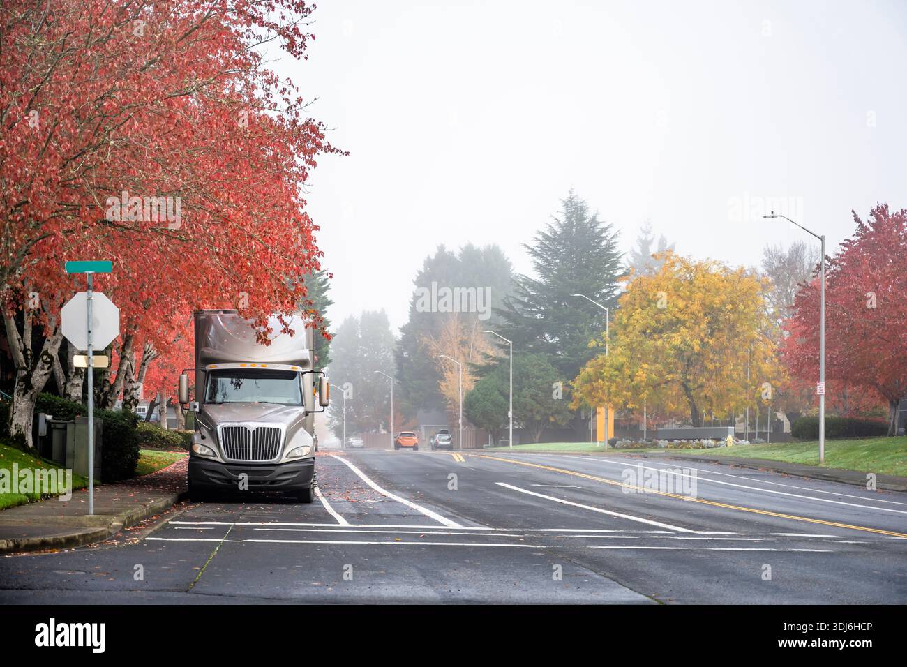 Beige Sattelzugmaschine mit großem Lkw in Industriequalität mit hohem Fahrerhausprofil und trockenem Auflieger für Lieferwagen, geparkt auf einer Stadtstraße mit rotem Herbstbaum Stockfoto