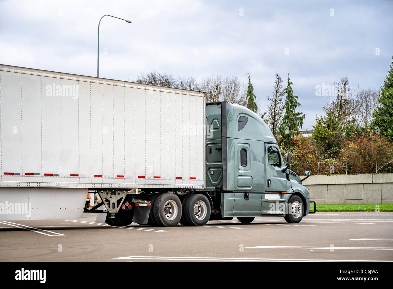 Grüne Sattelzugmaschine mit großem Lkw in Industriequalität mit verlängerter Fahrerkabine für den LKW-Fahrer und trockenem Anhänger mit Auflieger auf dem markierten Parkplatz Stockfoto