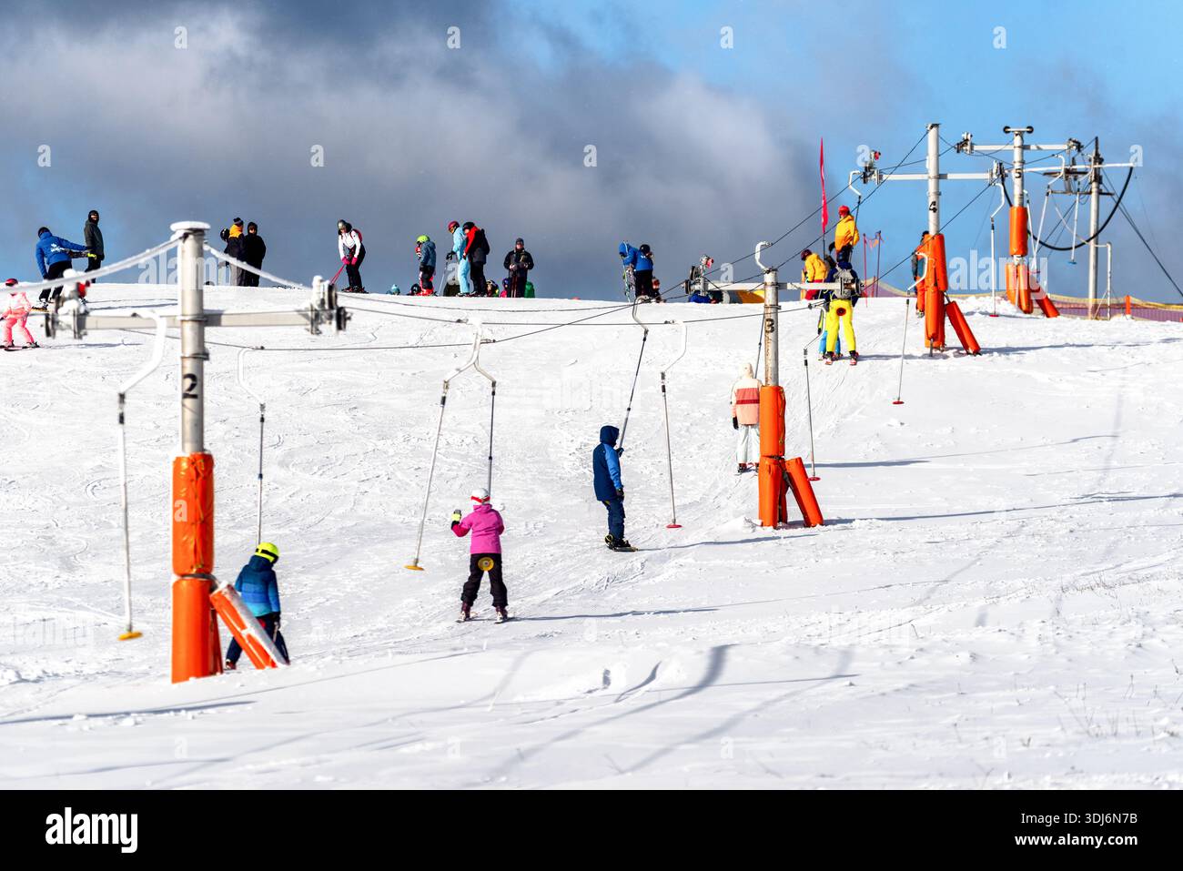 Ruzomberok, Slowakei - 30. Dezember 2025: Skifahrer mit Liften auf belebter Anfängerpiste im Skigebiet Malino Brdo, Wintererholung, Skifahren weniger Stockfoto