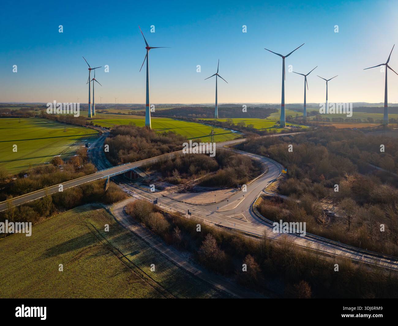 Luftaufnahme einer ländlichen Straßenkreuzung, umgeben von grünen landwirtschaftlichen Feldern und Wäldern, aus einer Drohnenperspektive. Die Szene zeigt einen Stockfoto