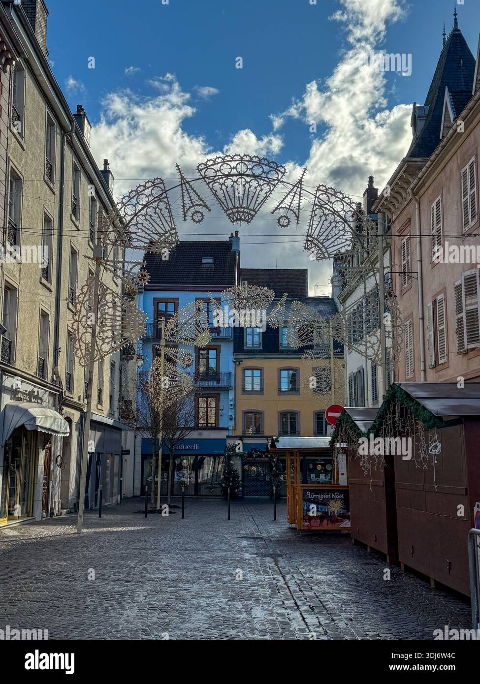 Festliche weihnachtsdekoration in Monbeliard, frankreich. Kunstvolle Lichterbögen hängen zwischen historischen Gebäuden und schaffen eine bezaubernde Atmosphäre - Smartphone-aufgenommenes Stockfoto