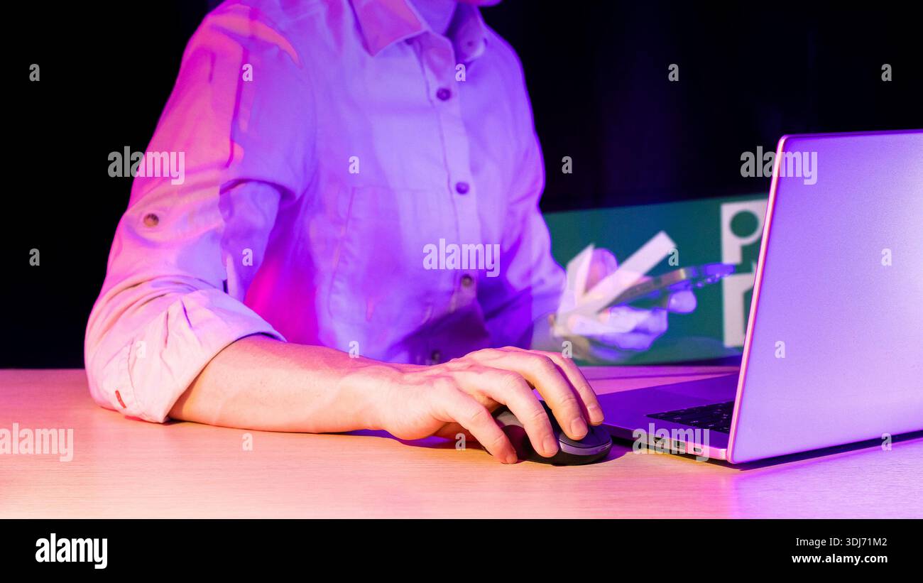 Nahaufnahme der Hand mit Computermaus, Laptop mit holografischem Pfeil, der auf das Symbol in Neonviolett zeigt. Stockfoto