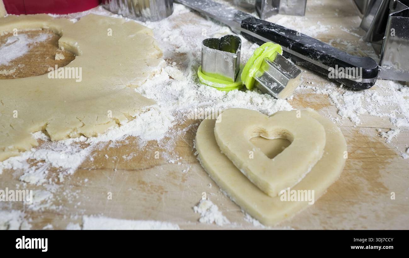 Zubereitung hausgemachter herzförmiger Kekse mit Teig, Mehl und Schneiden auf einem Holzbrett Stockfoto