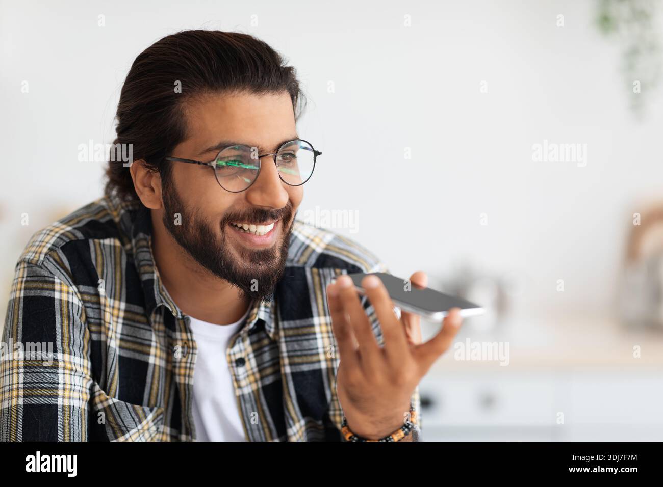 Hübscher bärtiger arabischer Mann in Brille, der eine Audiobotschaft aufzeichnet Stockfoto