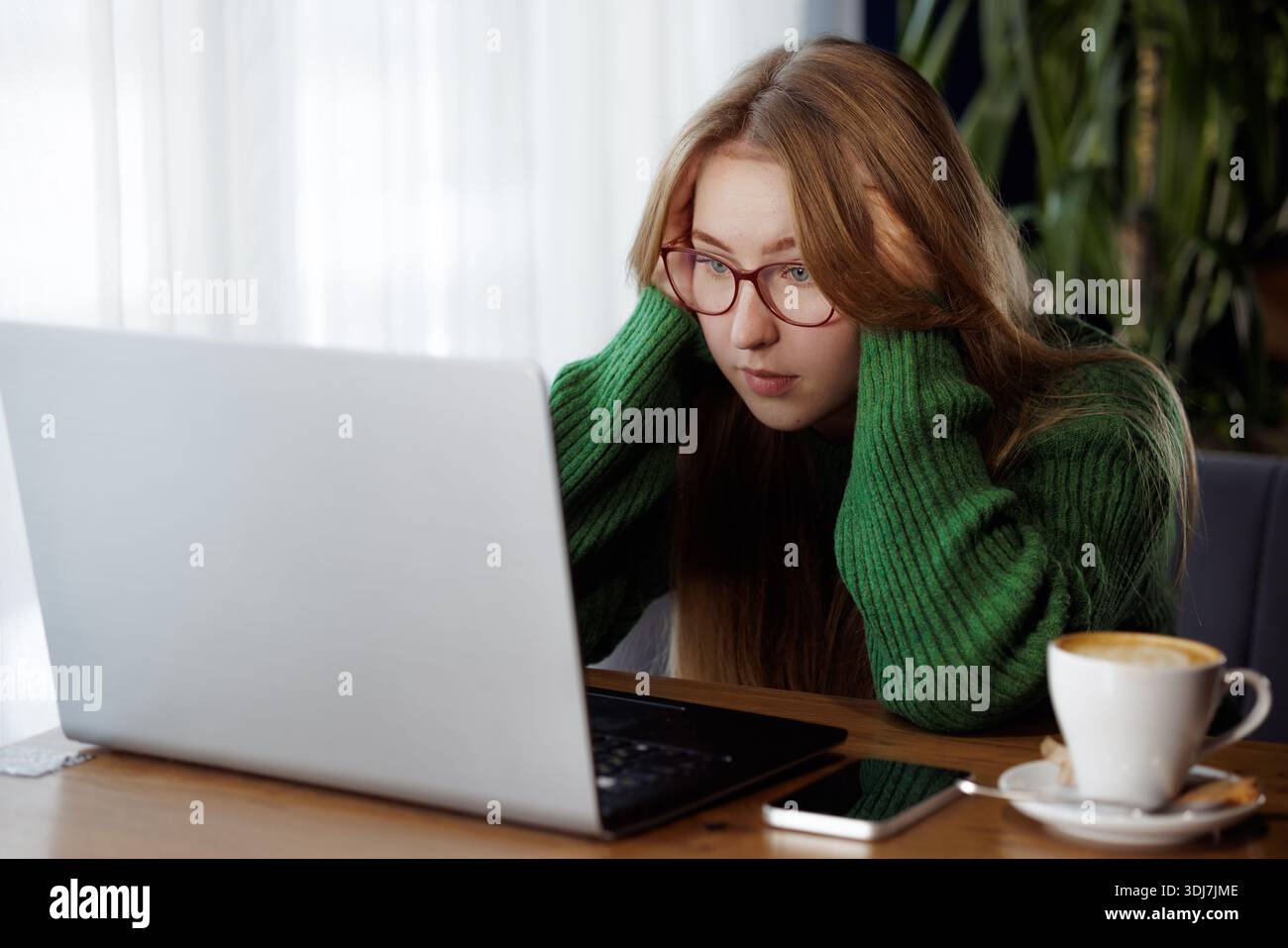 Frustrierte junge Frau, die auf den Laptop-Bildschirm schaut, während sie im Café arbeitet und mit technischen oder beruflichen Problemen konfrontiert ist. Stockfoto