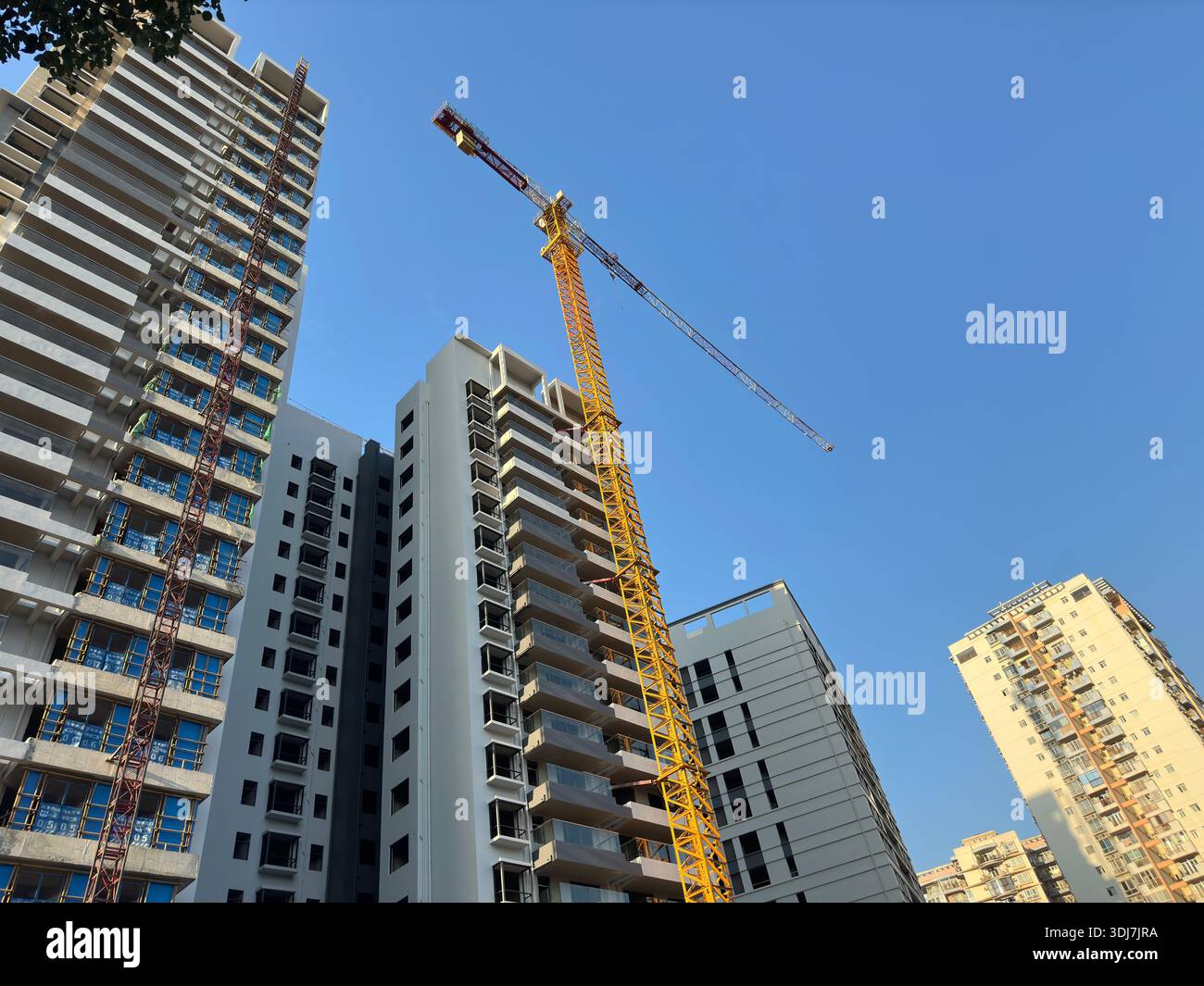 Bau von Wohnhochhäusern mit einem Kran vor klarem blauem Himmel - Smartphone-aufgenommenes Stockfoto