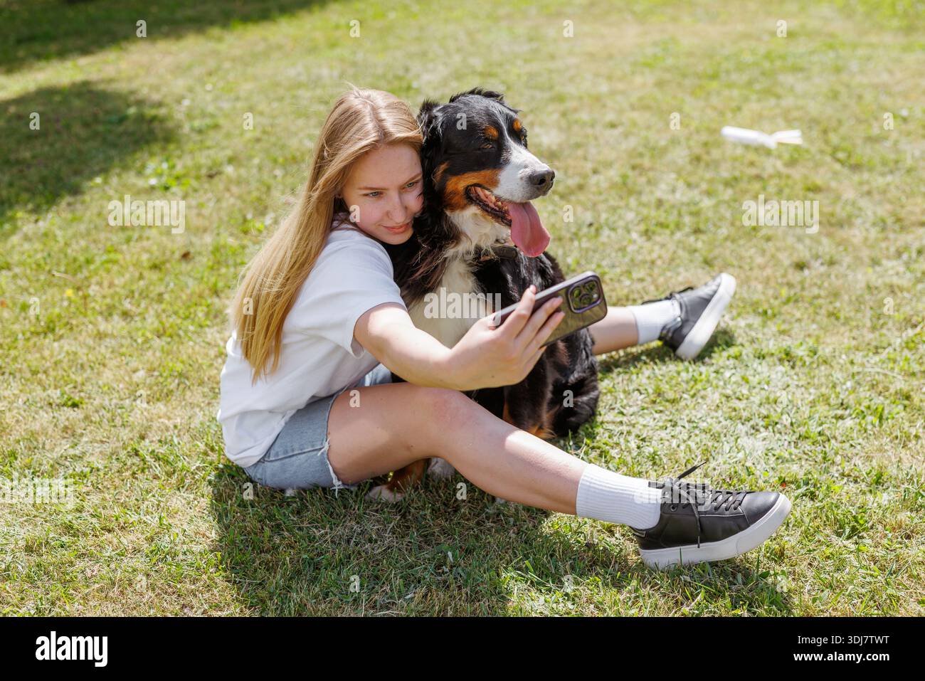 Eine Frau fängt freudig einen Moment ein, indem sie ein Selfie mit ihrem geliebten Hund auf dem Gras macht und beide eine glückliche und ehrliche Geste teilen Stockfoto