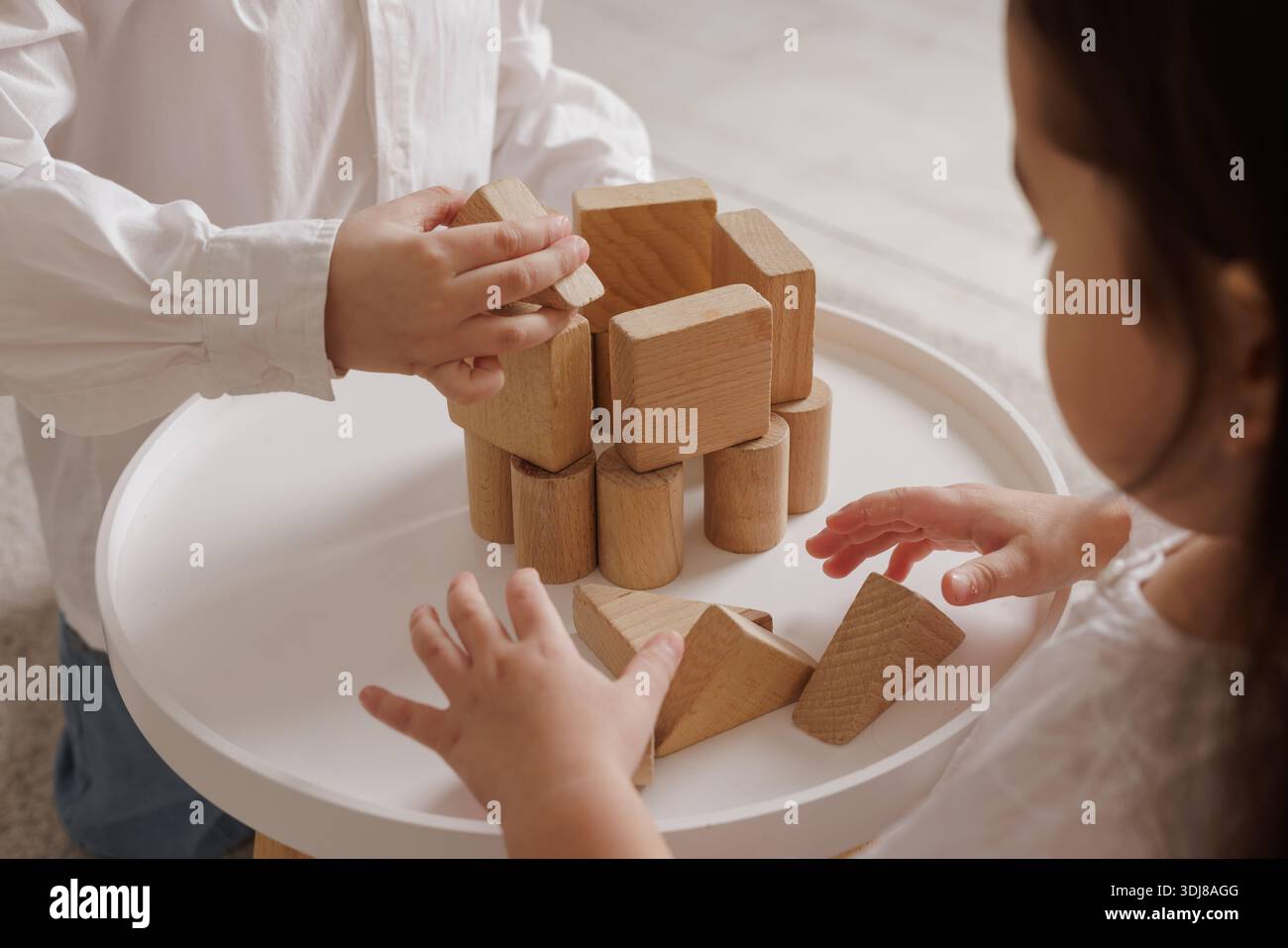 Kinder spielen mit Holzblöcken, bauen gemeinsam einen Turm auf einem weißen Tisch, spielen kreativ und lehrreich in einer gemütlichen Atmosphäre. Stockfoto