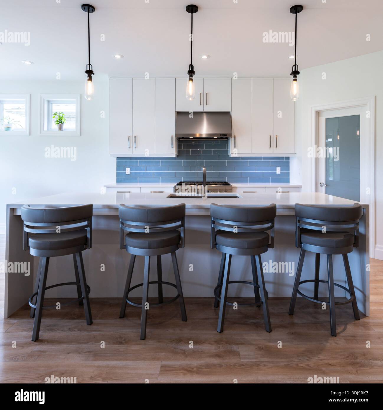 Helle, moderne Küche mit weißen Schränken, Inselsitzen, blauen Fliesen Backsplash und Pendelbeleuchtung in einem sauberen, offenen Wohnraum. Stockfoto