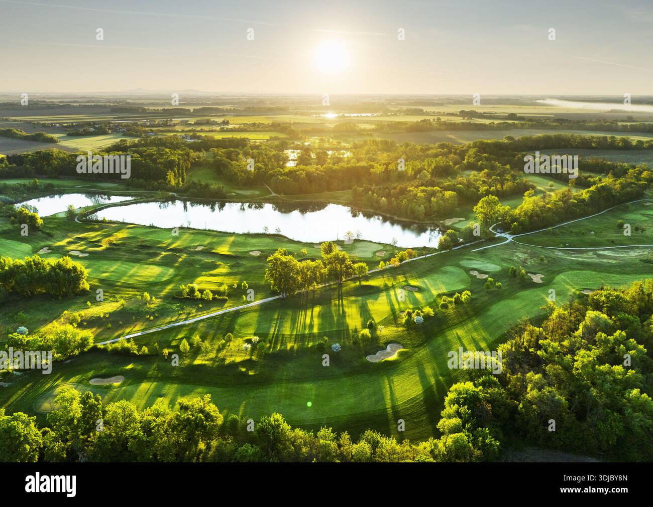 Panorama des Golfplatzes bei dramatischem Sonnenaufgang mit grünen Fairways und Wald Stockfoto