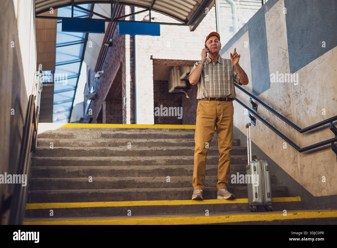 Der Senior Mann steht am Bahnhof und spricht mit dem Handy. Senioren reisen. Stockfoto