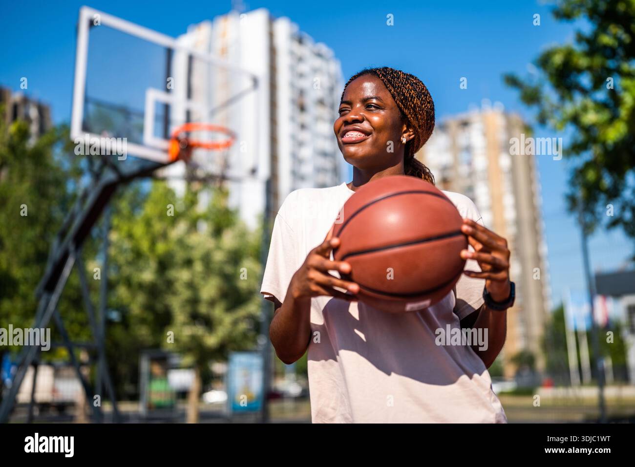 Afroamerikanische Spielerin hält einen Ball und lacht während des Sommertrainings. Aktiver Lifestyle und Stadtsport. Stockfoto