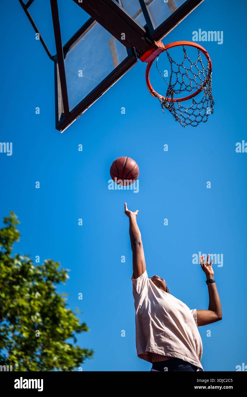Junge Frau, die Basketball allein auf dem Sportplatz übt, an sonnigen Tagen. Sie schießt auf Korb. Stockfoto