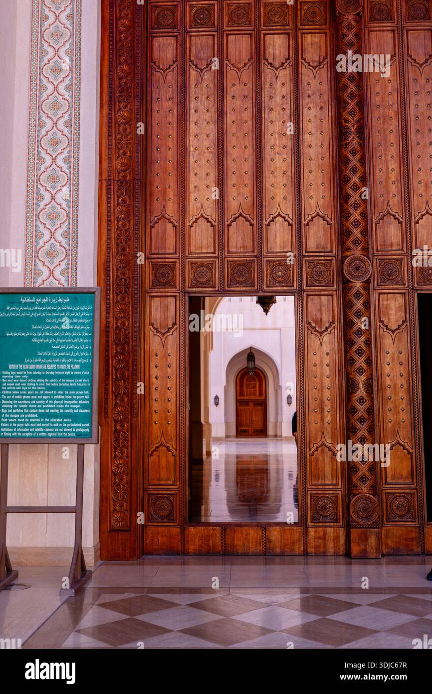 Kunstvoll verzierte Holztüren führen in eine Moschee in Salalah, Oman. Das warme, einladende Licht beleuchtet den polierten Boden und weiß Stockfoto