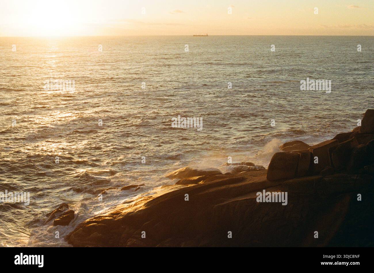 Sonnenuntergang über dem Meer mit Wellen, die gegen Felsen krachen Stockfoto