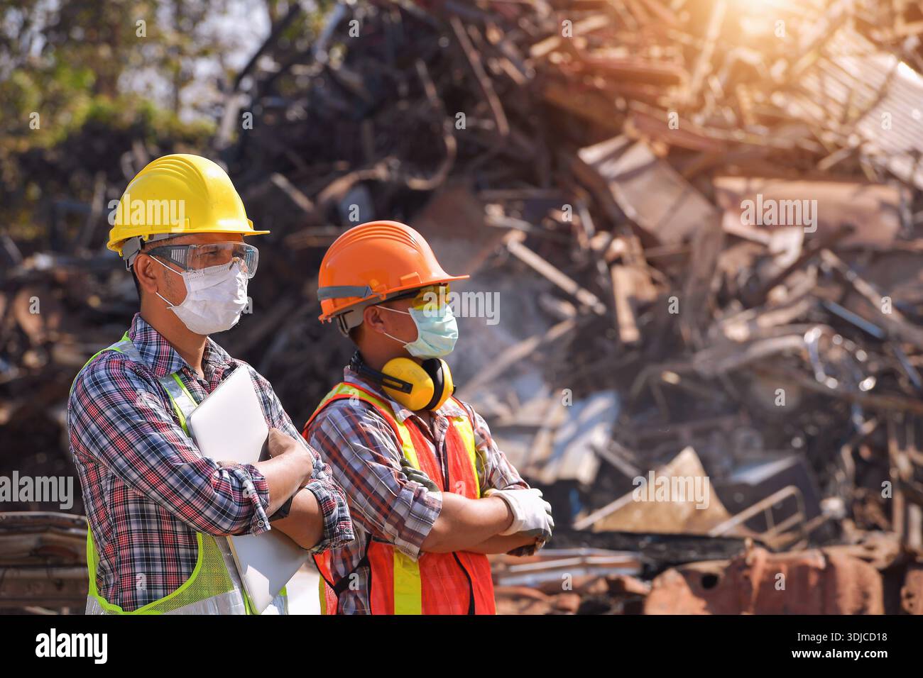 Zwei Handwerker, die Gesichtsmasken und Arbeitskleidung tragen, stehen nebeneinander in einem Schrottplatz in Thailand Stockfoto