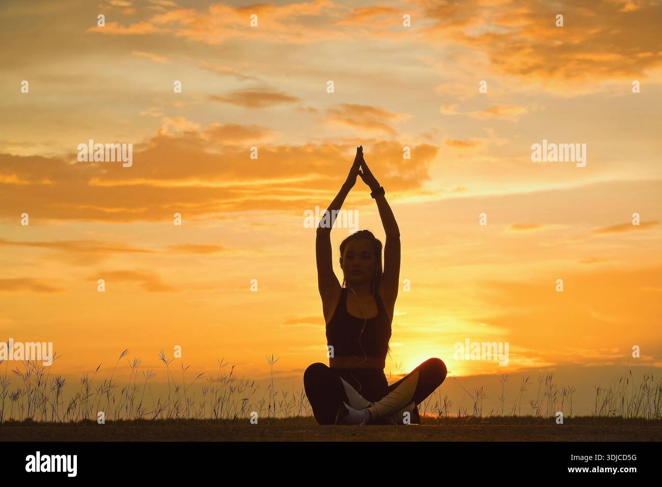 Silhouette einer Frau, die im Kreuz sitzt und ihre Arme in der Luft beim Sonnenuntergang in Thailand Yoga macht Stockfoto