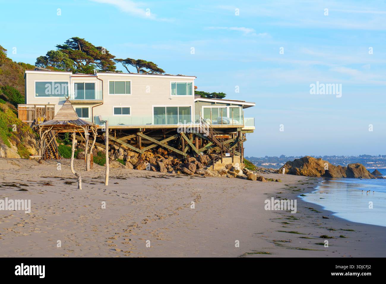 Modernes Strandhaus, architektonisch bedeutsam mit mehreren Glasbalkonen, gestützt von robusten Holzpfählen direkt über einem ruhigen, uncro Stockfoto