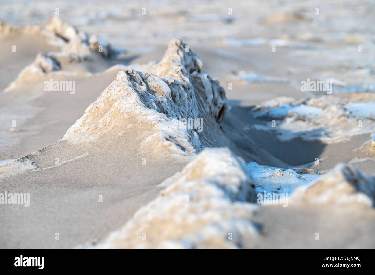 Gefrorene Sanddünen mit blauen Eisformationen am Ostseestrand im Winter. Natürliche Frostmuster schaffen abstrakte Texturen auf schneebedeckten Sandküsten-lan Stockfoto