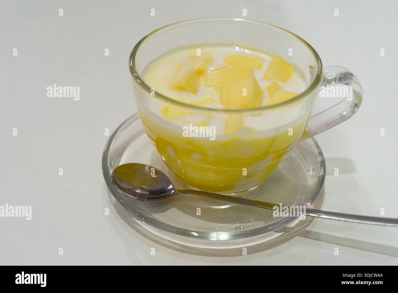 Eine Glasschale gefüllt mit glattem Mangojoghurt, gekrönt mit frisch geschnittenen Stücken reifer Mango Stockfoto
